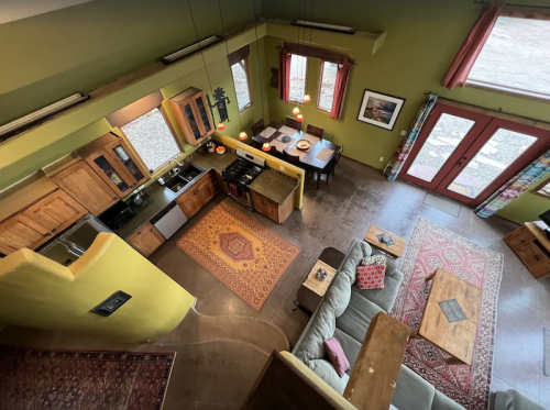 Aerial view of a cozy, modern kitchen and dining area with wooden cabinets, a sofa, and colorful rugs.