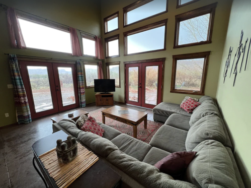 Cozy living room with large windows, a sectional sofa, coffee table, and a TV, overlooking a scenic outdoor view.