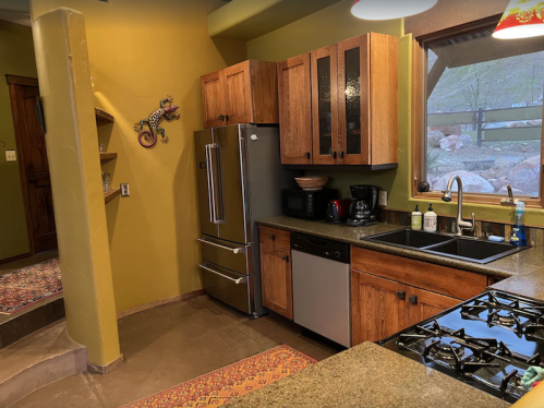 A modern kitchen with wooden cabinets, stainless steel appliances, and a stone countertop, featuring a colorful rug.