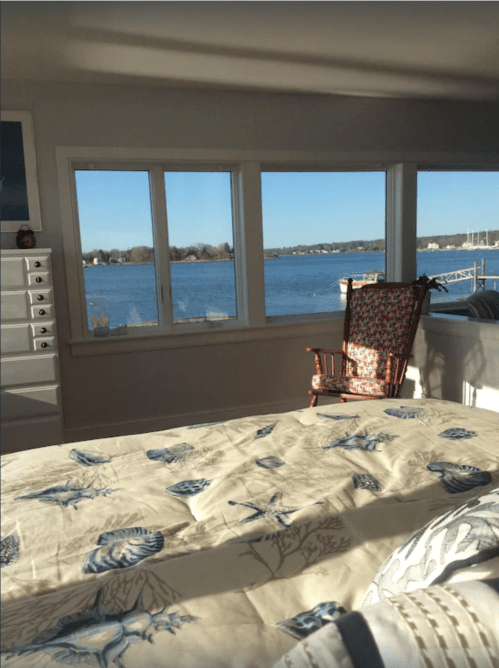 A cozy bedroom with a bed and a rocking chair, featuring large windows overlooking a serene lake.