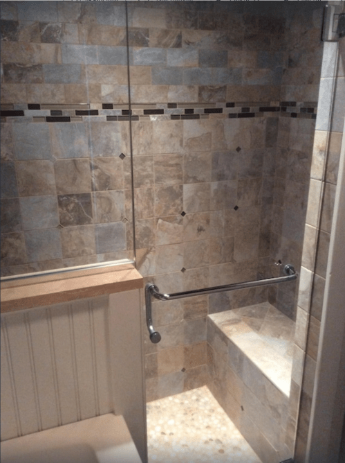 A modern shower with tiled walls, a built-in bench, and a grab bar, featuring a pebble floor and glass enclosure.
