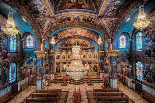 Interior of a beautifully decorated church featuring ornate chandeliers, colorful murals, and stained glass windows.