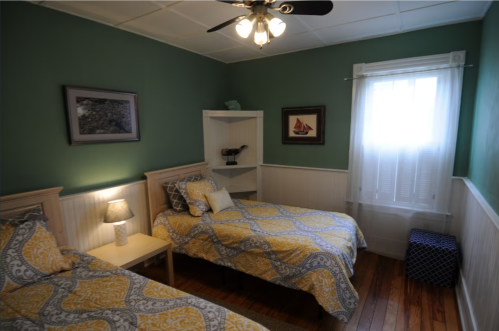 Cozy bedroom with two twin beds, green walls, a window with sheer curtains, and a small bookshelf.