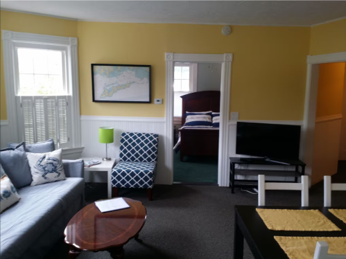 Cozy living room with yellow walls, a blue sofa, a coffee table, and a view into a bedroom.