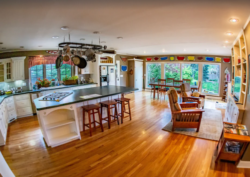 Spacious kitchen with an island, wooden floors, and large windows overlooking a garden. Cozy seating area included.