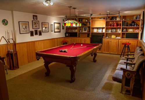 A cozy game room featuring a red pool table, wooden shelves, framed photos, and comfortable seating.