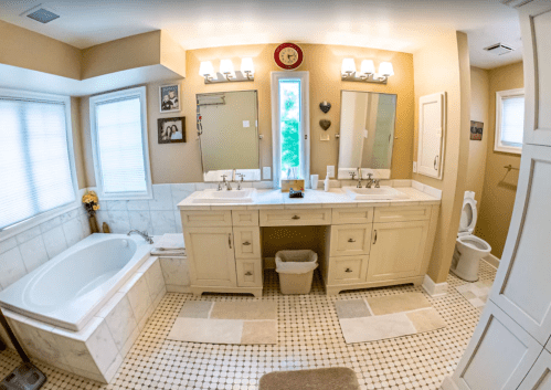 Spacious bathroom with double sinks, a bathtub, and natural light from windows, featuring neutral tones and tiled flooring.