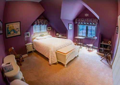 Cozy purple bedroom with a bed, window, and vintage furniture, featuring soft lighting and a warm atmosphere.