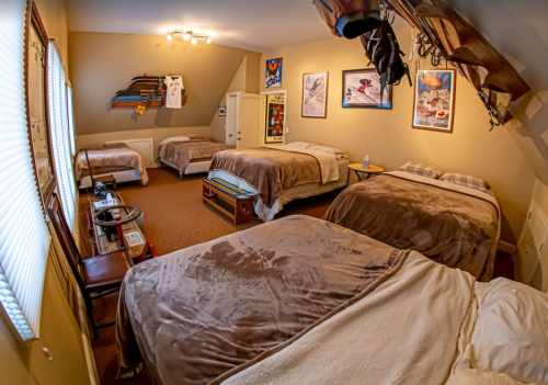 Cozy attic room with four beds, warm decor, and vintage ski posters on the walls.