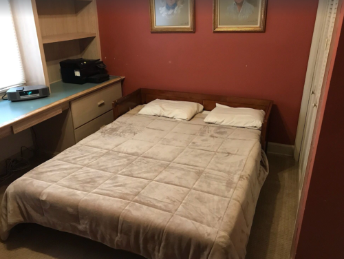A simple bedroom with a double bed, two pillows, and a wooden frame, against a red wall with framed pictures.