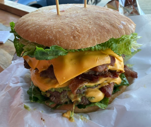 A towering burger with multiple beef patties, melted cheese, bacon, and lettuce, served on a large bun.