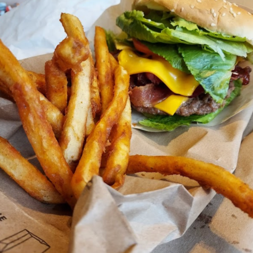 A juicy cheeseburger with lettuce and bacon next to a serving of crispy French fries on brown paper.