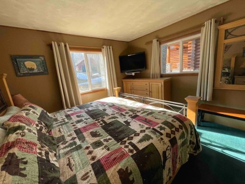 Cozy bedroom with a quilted bedspread, wooden furniture, and windows letting in natural light.