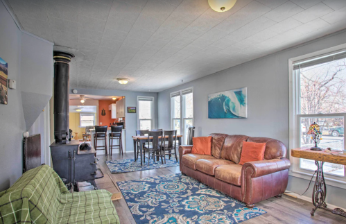 Cozy living room with a leather sofa, patterned rugs, and a wood stove, leading to a dining area with a kitchen in the background.