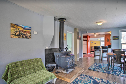 Cozy living space with a wood stove, green sofa, and dining area, featuring blue rugs and warm lighting.