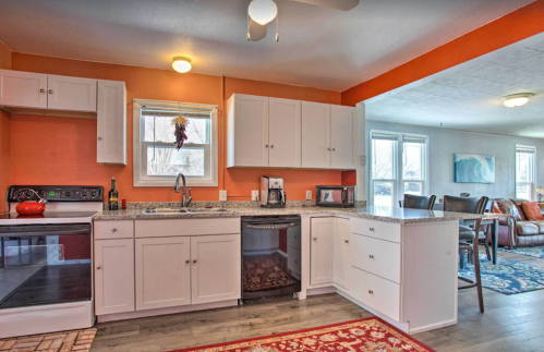 Bright kitchen with white cabinets, granite countertops, and an orange accent wall, featuring a cozy living area in the background.
