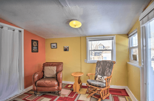 Cozy room with a leather chair, rocking chair, small table, and colorful walls, featuring large windows for natural light.