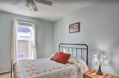 Cozy bedroom with a metal bed, floral quilt, decorative pillows, a lamp, and a window letting in natural light.