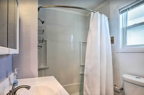 A clean bathroom featuring a shower with a white curtain, sink, and window for natural light.
