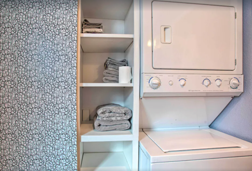 A laundry area featuring a stacked washer and dryer next to neatly folded towels on shelves.