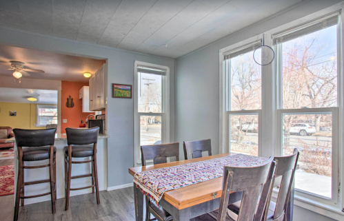 A cozy dining area with a wooden table, chairs, and large windows, overlooking a sunny outdoor view.