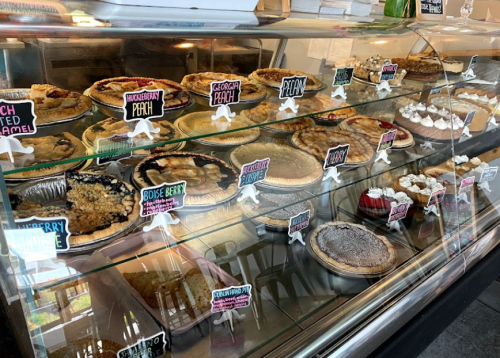 A display case filled with various pies, each labeled with colorful signs, showcasing flavors like peach, blueberry, and more.