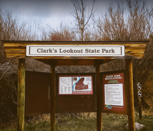 Sign for Clark's Lookout State Park, featuring park regulations and a map, surrounded by bare trees.