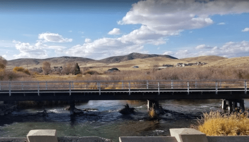 A scenic view of a river flowing under a bridge, with rolling hills and clouds in the background.