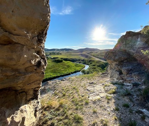 A scenic view from a rocky outcrop overlooking a winding river and lush green fields under a bright blue sky.