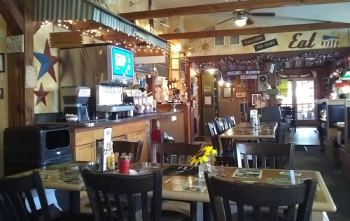 Cozy restaurant interior with wooden tables, chairs, and a bar area, decorated with lights and vintage signs.