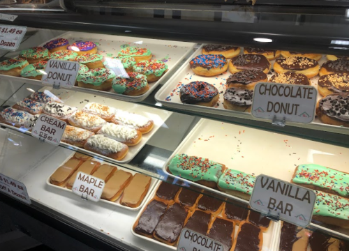 A display case filled with various colorful donuts, including chocolate, vanilla, and cream varieties, with price tags.