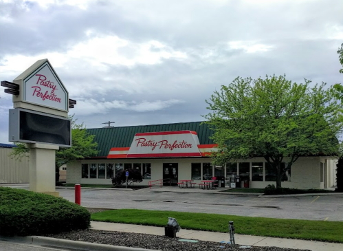 A bakery named "Pastry Perfection" with a green roof and outdoor seating, surrounded by trees and cloudy skies.