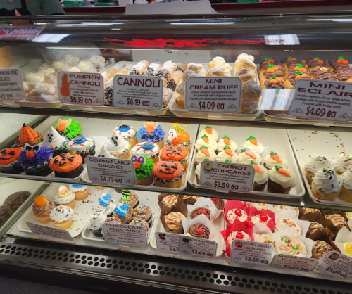 A display case filled with various colorful desserts, including cupcakes, cannoli, cream puffs, and eclairs.