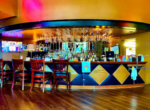 A stylish bar with a polished counter, shelves of liquor, and bar stools, set in a warm, inviting atmosphere.