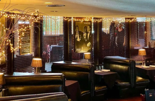 Cozy restaurant interior with dim lighting, black leather seating, and decorative string lights.