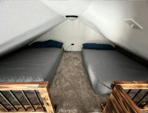Cozy attic bedroom with two twin beds, carpeted floor, and sloped ceiling.