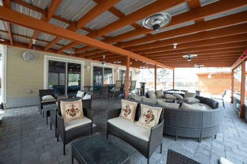 A spacious outdoor patio with wicker furniture, decorative pillows, and a covered roof, featuring a cozy seating area.
