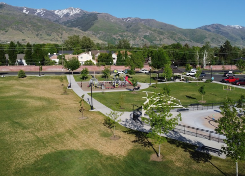 Aerial view of a park with playground equipment, green grass, trees, and mountains in the background.