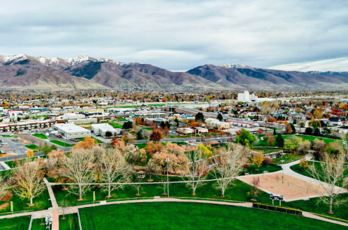 Aerial view of a town surrounded by mountains, featuring parks, trees, and a mix of residential and commercial buildings.
