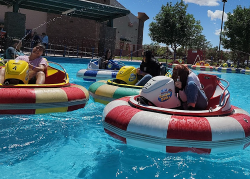 A group of people enjoying bumper boats in a bright blue pool on a sunny day.