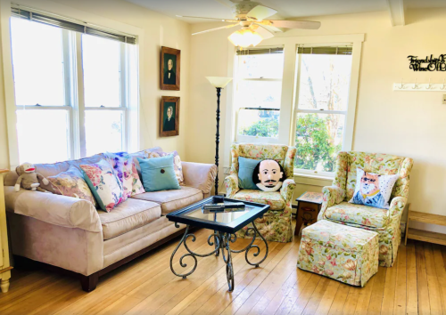 Cozy living room with floral furniture, a coffee table, and large windows letting in natural light.