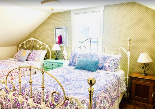 Cozy bedroom with two beds, floral bedding, a green dresser, and warm lighting under a sloped ceiling.