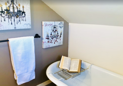 A cozy bathroom corner featuring a bathtub, an open book on a rack, a towel, and decorative chandelier artwork.