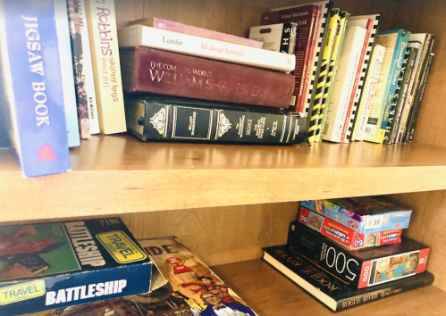 A wooden shelf filled with various books, including cookbooks, novels, and board games.