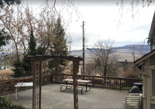 A wooden deck with picnic tables overlooks a cloudy landscape and distant mountains, surrounded by bare trees.