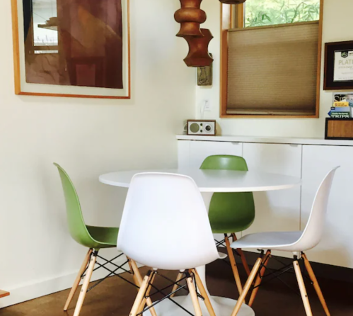 A small dining area featuring a round table with four chairs, two white and two green, and a wooden pendant light.