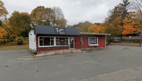 A small red building with a black sign reading "T's Cafe," surrounded by autumn trees and an empty parking lot.
