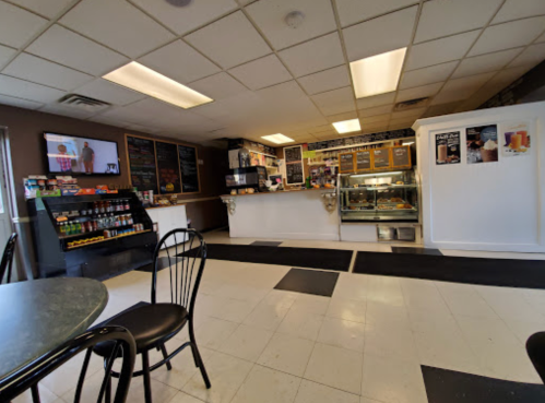 A cozy café interior featuring a counter, display case, menu boards, and seating area with black chairs.