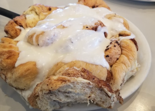 A close-up of a cinnamon roll topped with creamy white icing on a white plate.