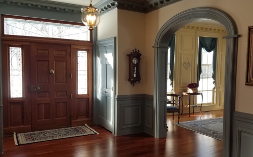 A spacious entryway with a wooden door, elegant archway, and a cozy sitting area with a clock and decorative accents.